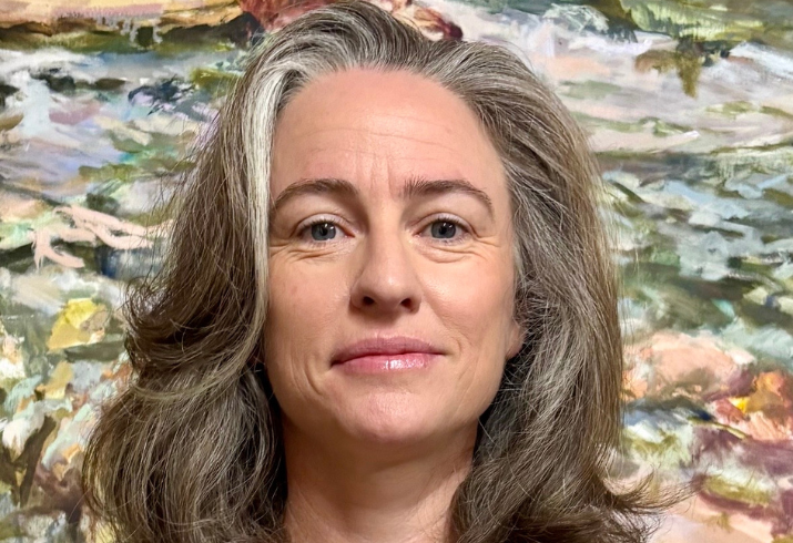 A woman stands against a floral background smiling