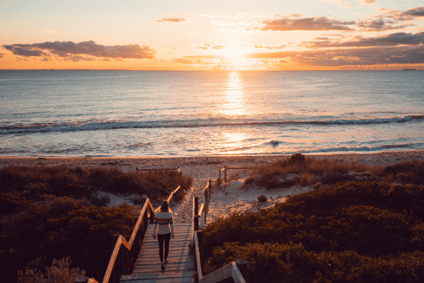 Woman walks down wooden path to the ocean