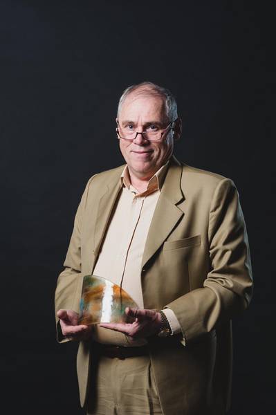 Dr Peter Van Maarseveen standing with glass award.