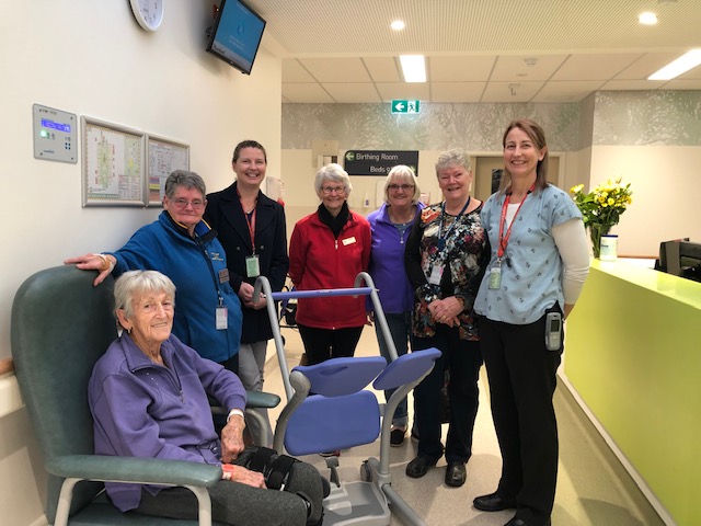 Several staff and patients around a steady Sara, a mobility support trolley for the elderly.