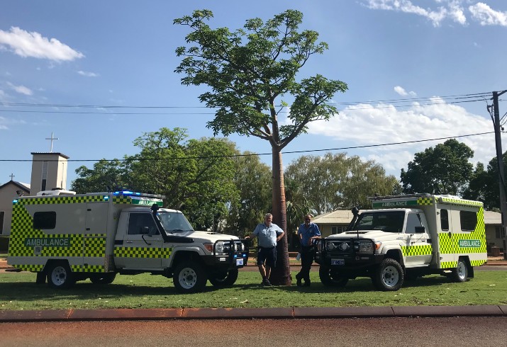 Two health staff members standing beside two new 4WD ambulances 