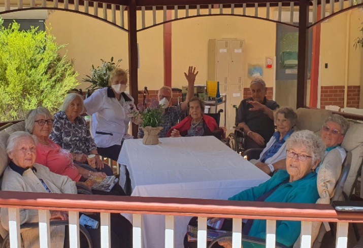 Ten elderly residents sit with staff under gazebo 