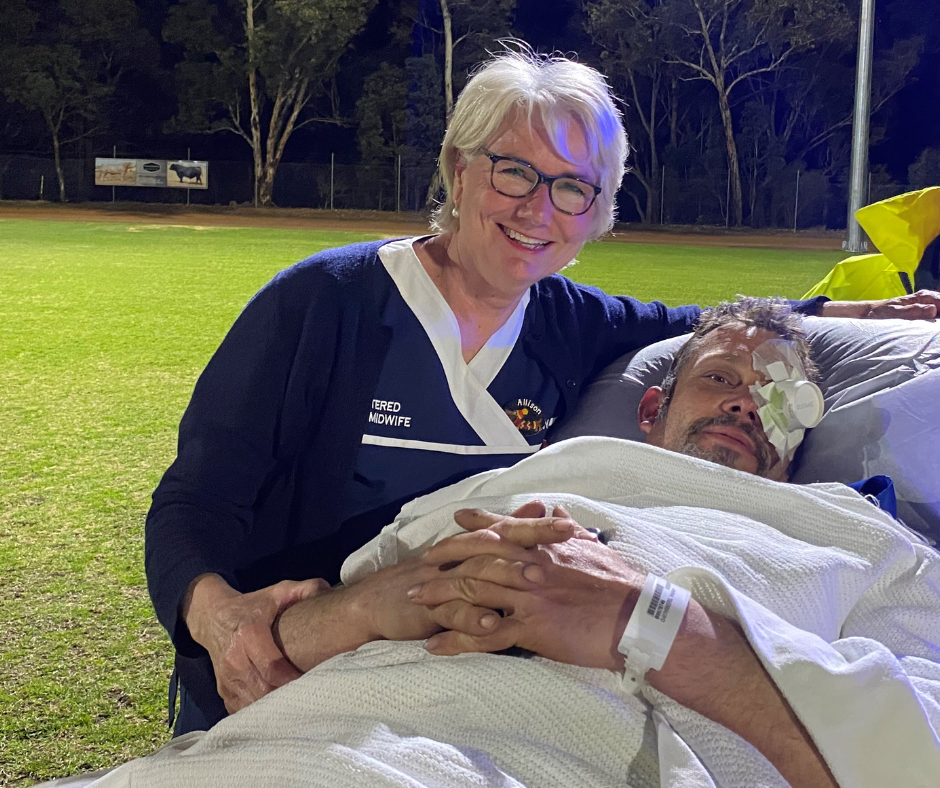 A nurse stands with a patient on a gurney with his eye covered, they are on an oval awaiting helicopter transfer