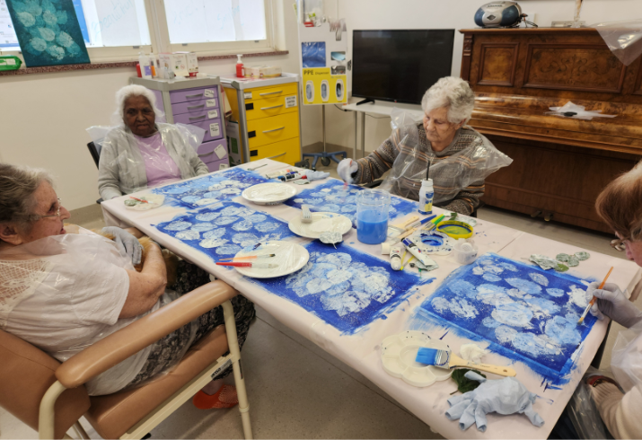A group of elderly residents sit around a large table working on art projects