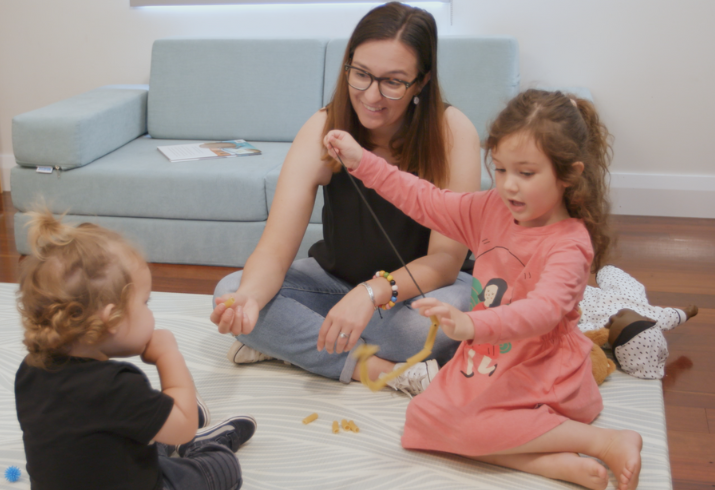 Two children on the floor with a parent playing with toys.