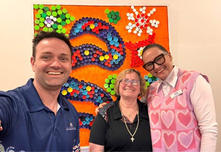Three people stand in front of a brightly coloured artwork smiling.