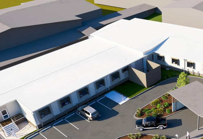A computer generated rendering of a new hospital ward looking down from a bird's eye view, the building is long and white with windows along the side fronting a neat car park.