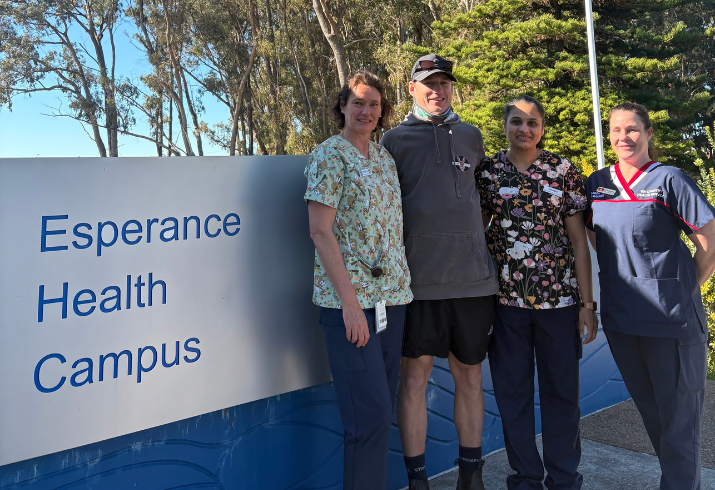 Alex (patient) standing with three nurses next to Esperance Health Campus sign.