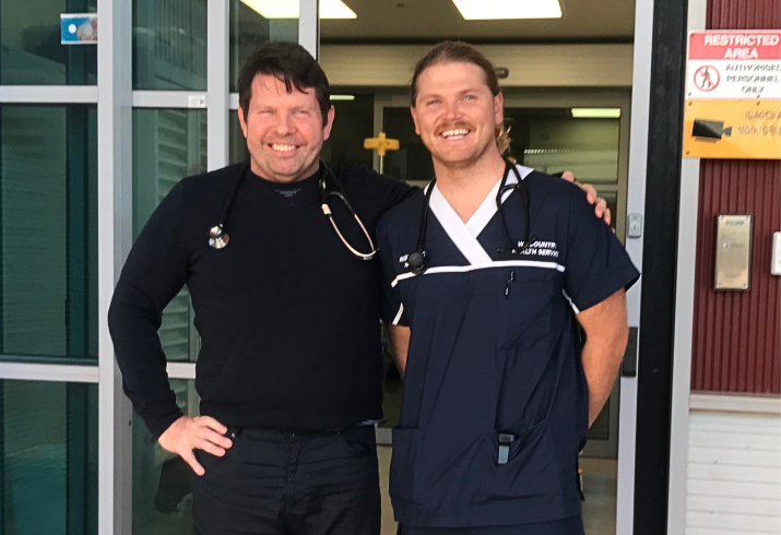Doctor and nurse standing in front of hospital entry.