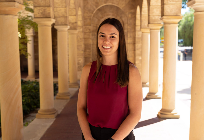 Woman in red shirt standing in an archway smiling at camera.