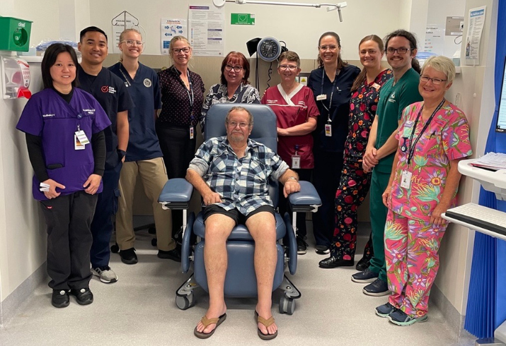 Group of staff standing around and behind a man in a treatment chair.