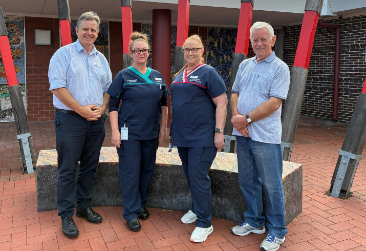 Two men in business casual attire standing with two nurses in scrubs outside a building.