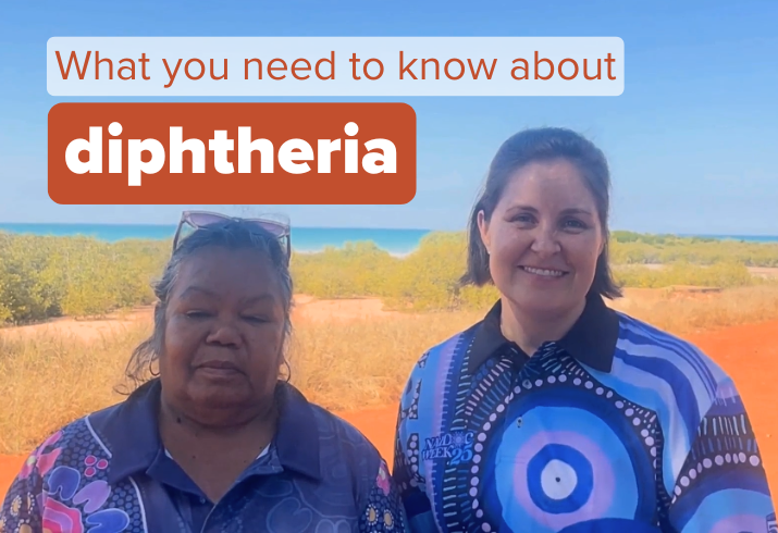 Two women in colourful polo shirts with Aboriginal artwork standing in front of Kimberley beach, showing red dirt, green trees and blue ocean.