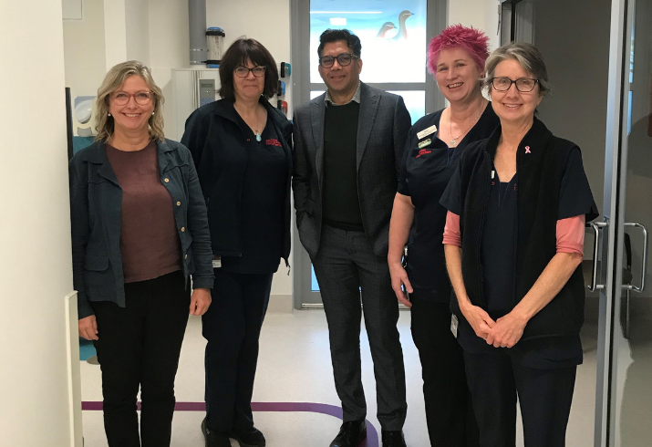 A group of nurses and clinical trials specialists and one male doctor stand in a hospital hallway smiling