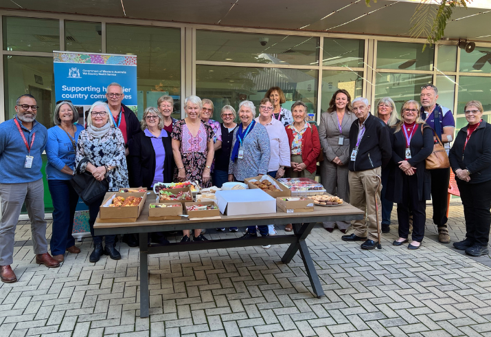 Large group of volunteers standing around a table of afternoon tea food.