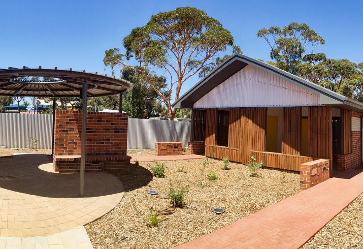 A bright residential building with a brick path leading to it and a rotunda with a small garden between