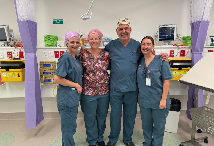 A male doctore and three female nurses in scrubs stand together smiling in a hospital room 