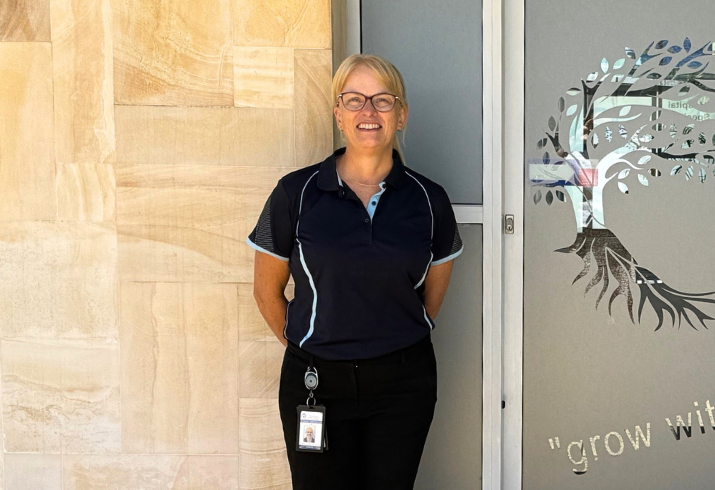 Women with blonde hair and glasses standing in front of building entrance.