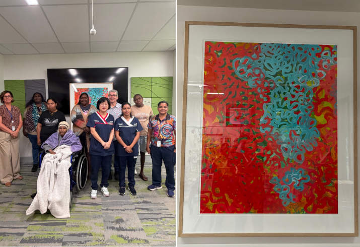 A group of people stand together in front of a brightly coloured artwork, some are nurses and hospital workers, some are Aboriginal family members with an elderly woman in a wheelchair in front