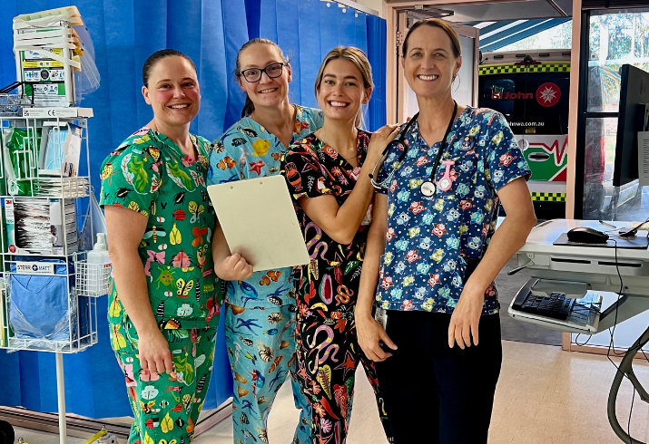 Four nurses in colourful scrubs stand in a hospital ward.