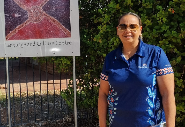 Woman in sunglasses and polo shirt with Aboriginal artwork standing outdoors in front of a tree.