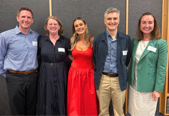 Five people standing in a line posing for a photo, with Michaela in the centre wearing a red dress.
