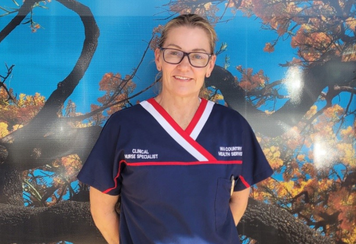 Female nurse in scrubs with glasses standing in front of a colourful wall.