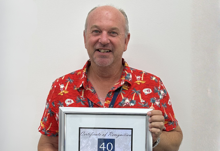 Man in red shirt holding up a framed certificate of achievement.