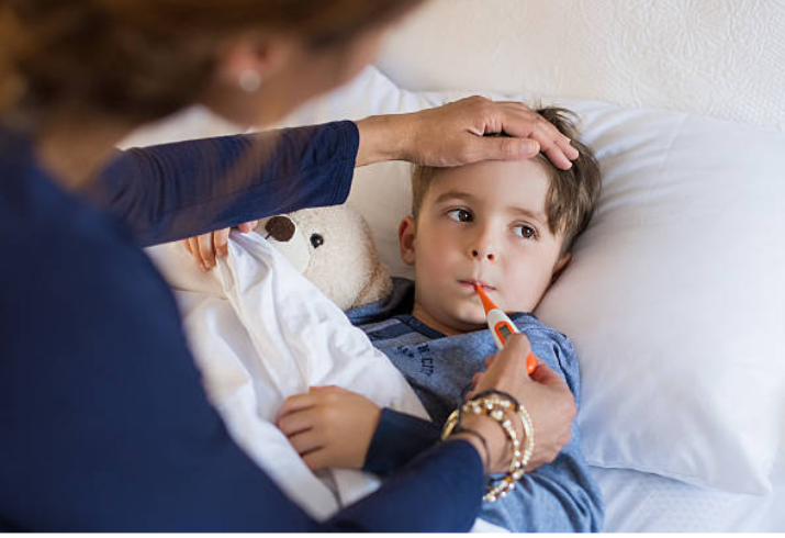 Image of a small child in bed having their temperature taken by an adult with a thermometer.
