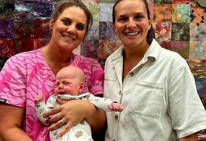Nurse in pink scrubs holding baby standing next to mother.